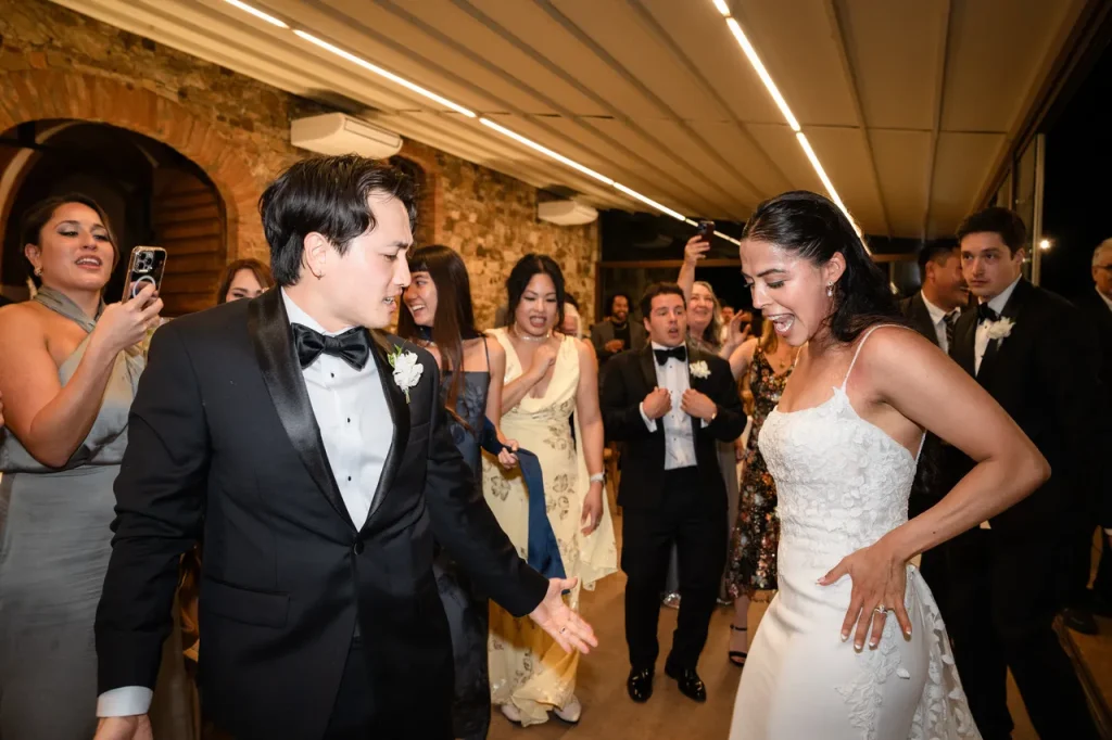 A bride and groom in formal attire dance joyfully among guests at an elegant wedding at Le Filigare Tuscany, surrounded by the charm of a vineyard venue in the Chianti hills.